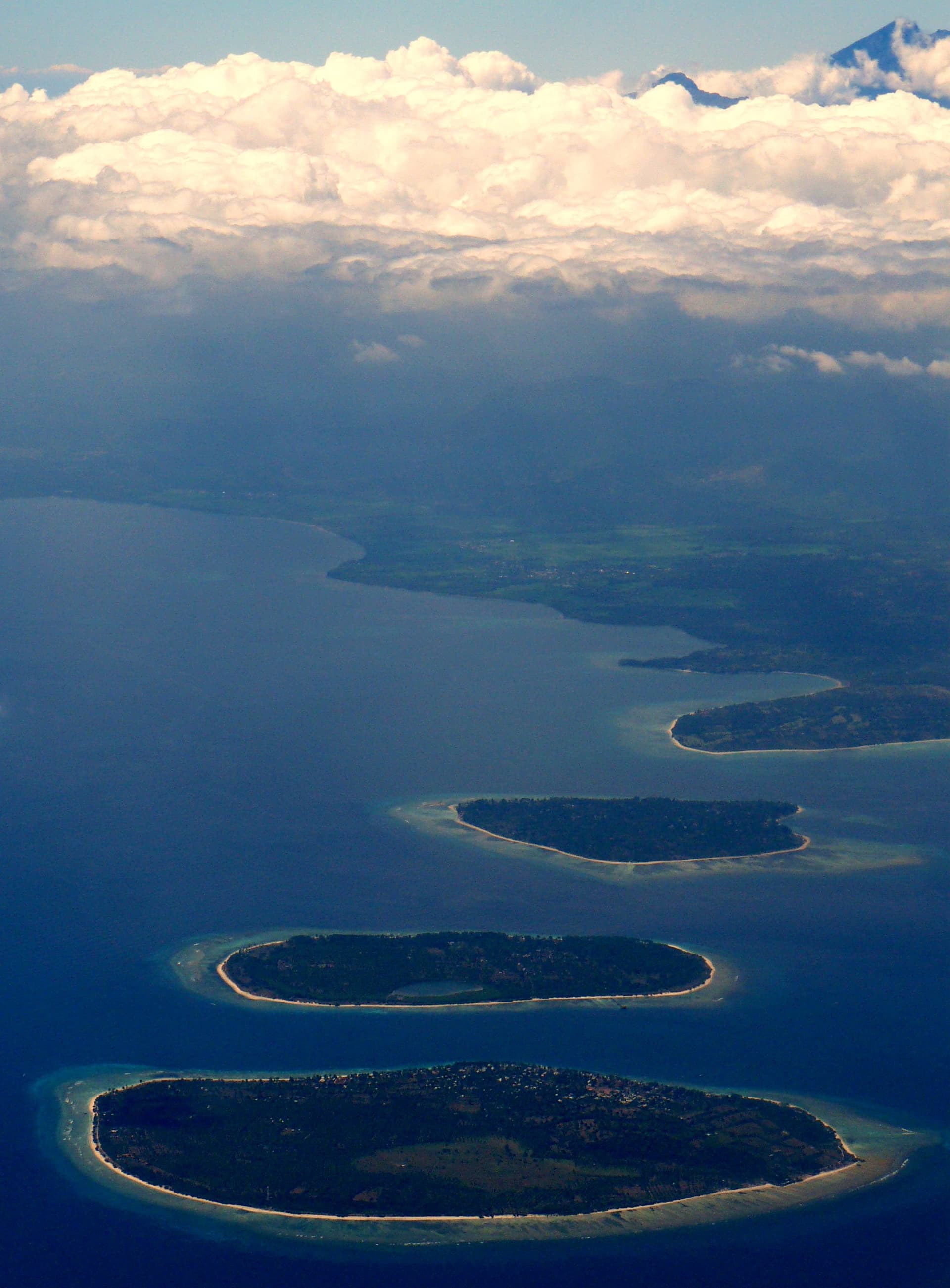 The three Gili Islands seen from a plane, with Mount Rinjani rising above the clouds