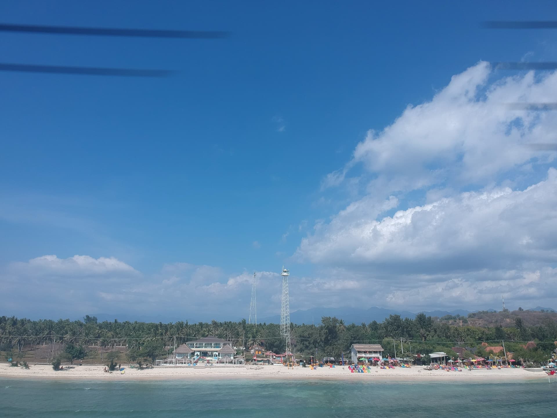 Gili Trawangan shoreline and lighthouse seen from a boat under a big cloudy sky
