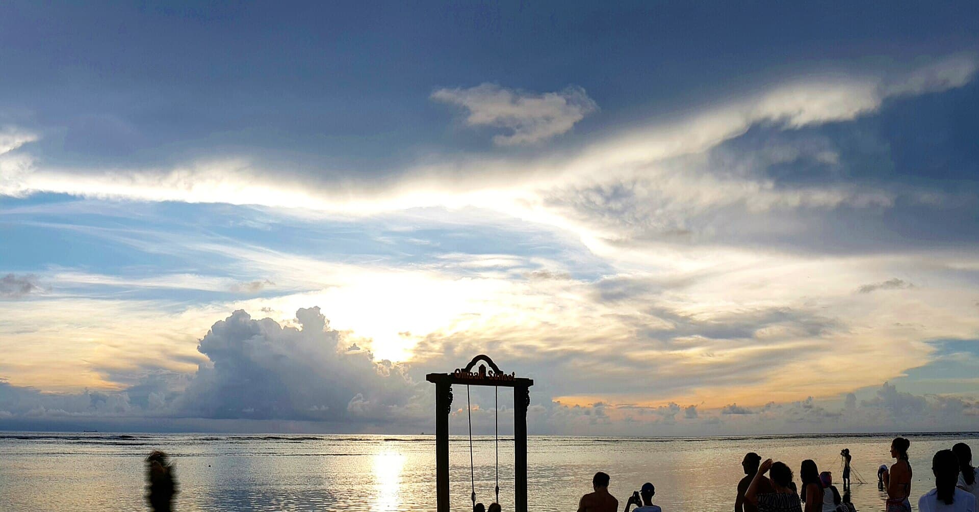 Silhouette of a beach swing in the sea at sunset, people on the shore