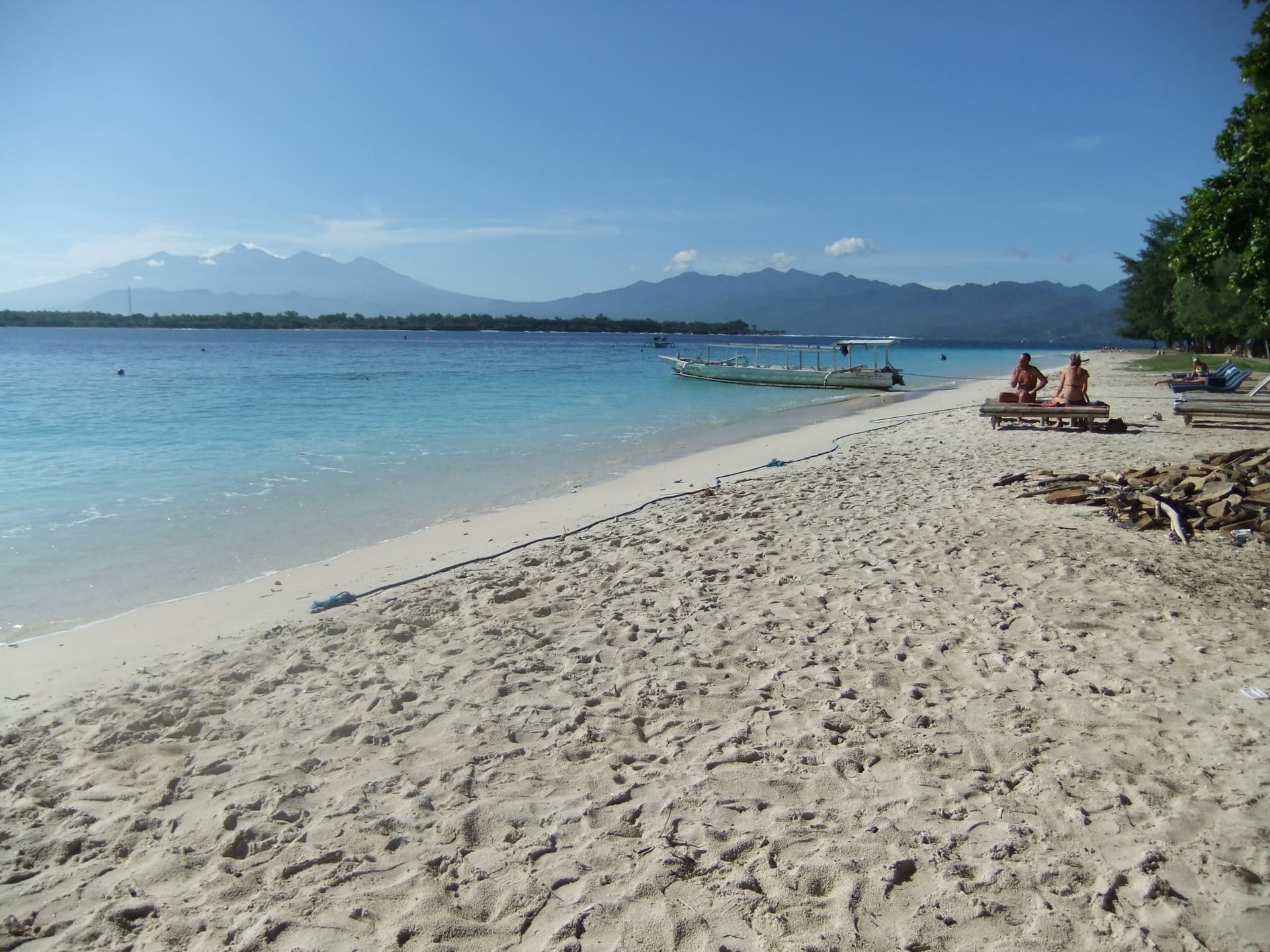 White-sand beach and turquoise water on Gili Trawangan, boats offshore and Lombok on the horizon