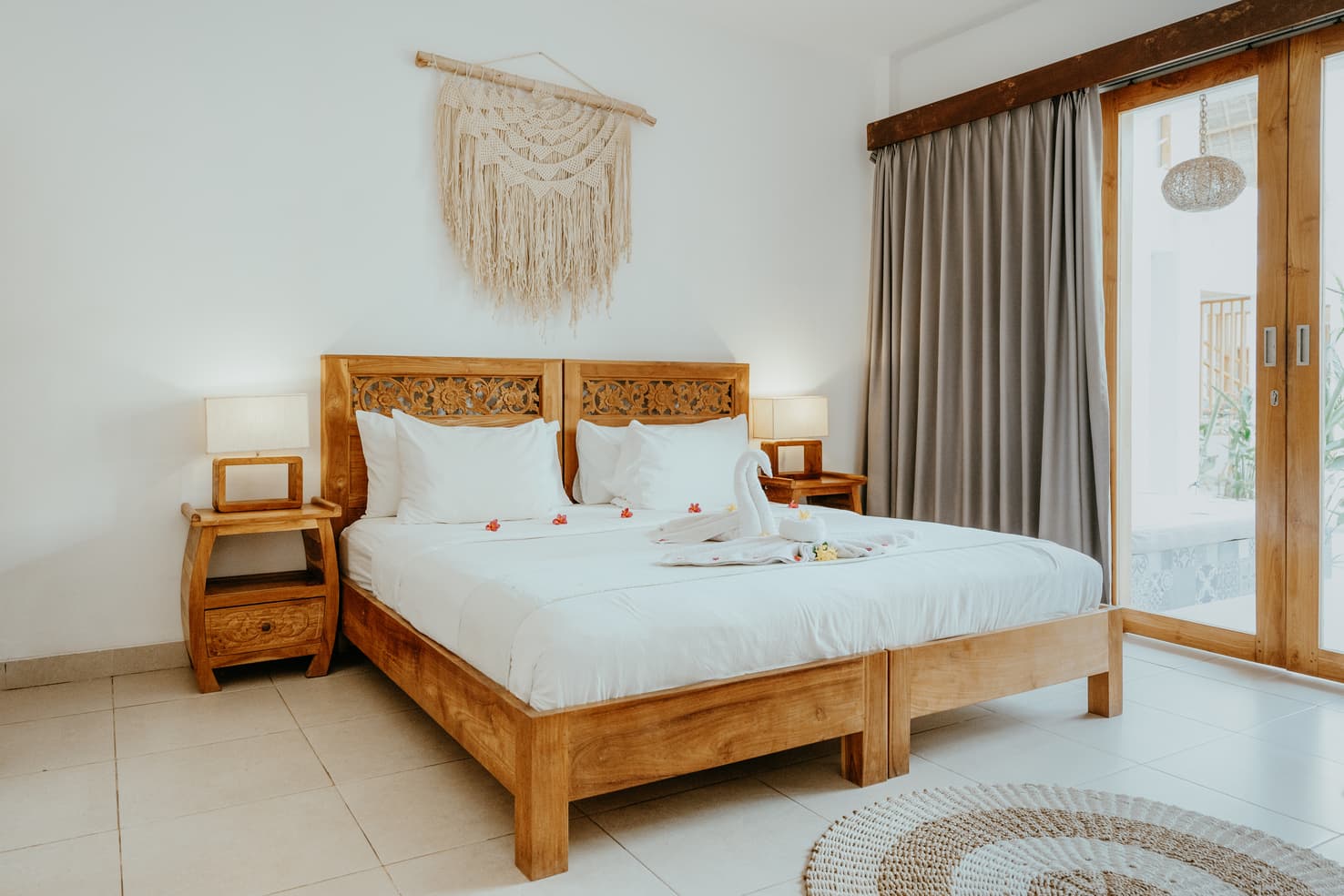 Bright hotel room with a wooden double bed, macramé wall hanging and glass door