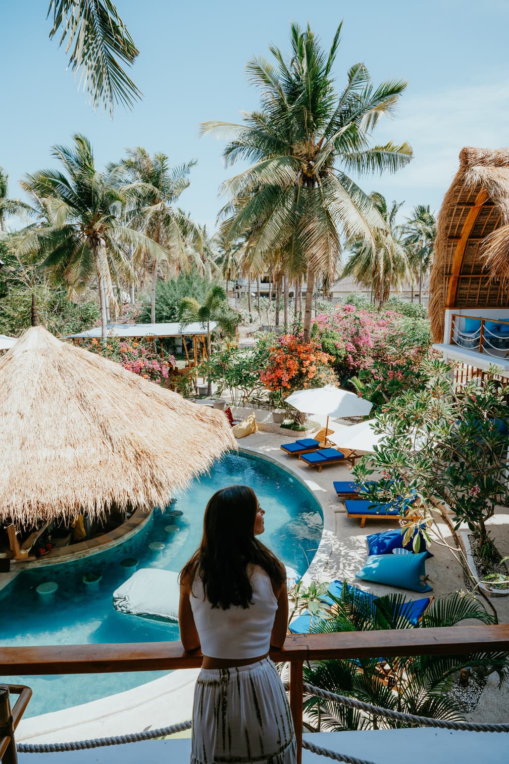 Guest on a balcony overlooking a resort pool, thatched roofs and palm trees