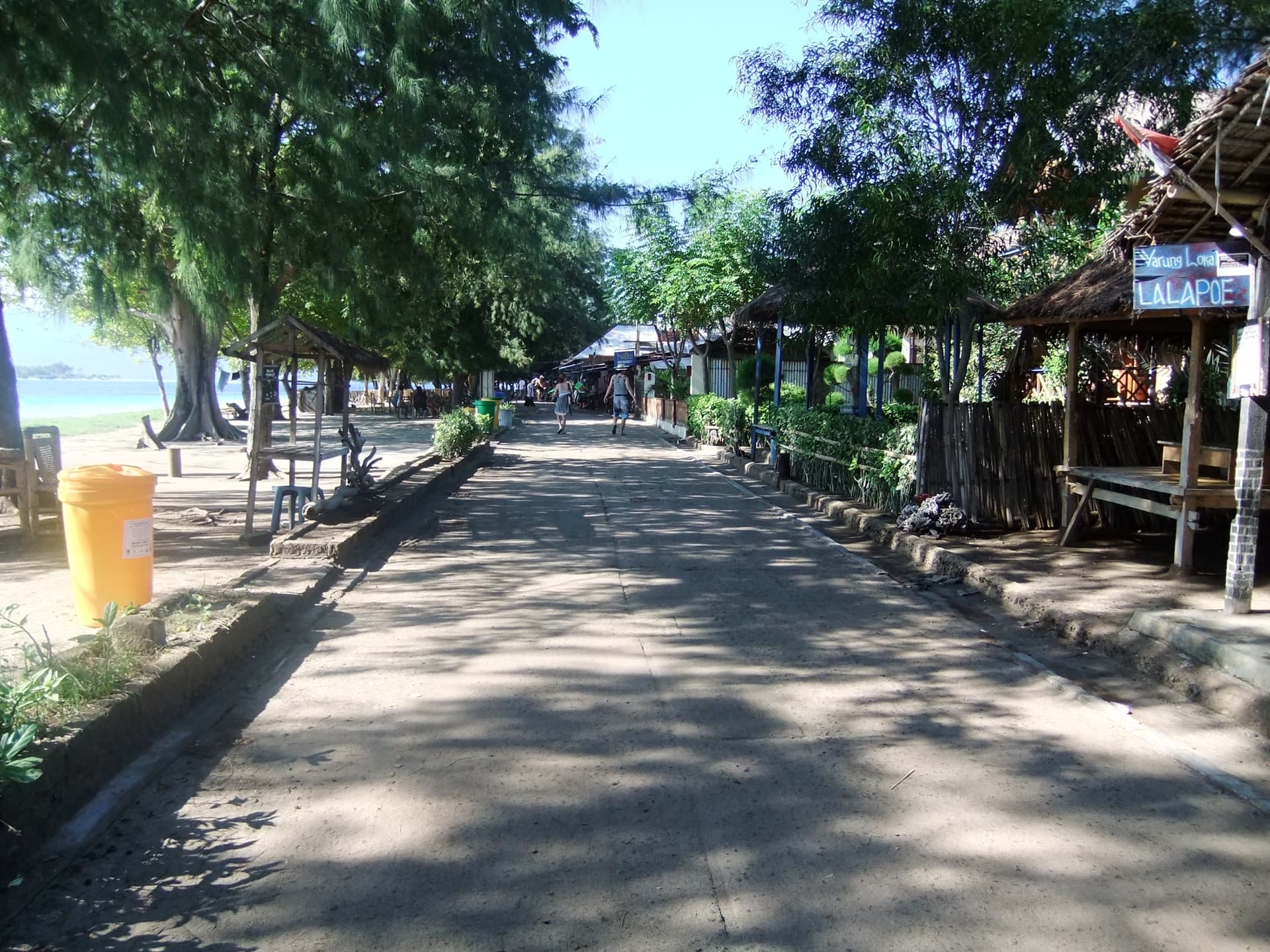 Shaded sandy main street on Gili Trawangan, lined with trees and stalls